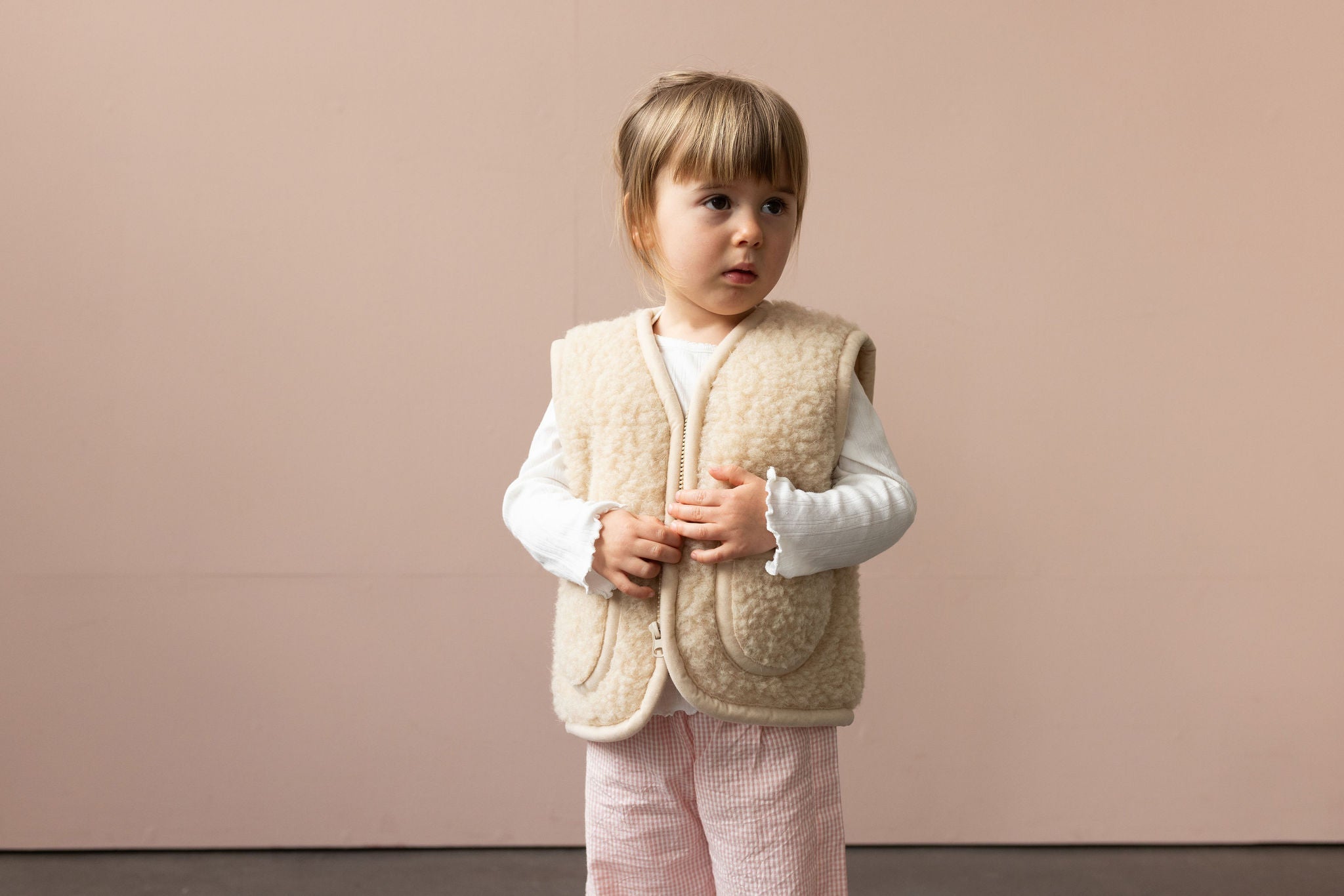 Zwei Kinder in beigen und braunen Wollwesten umarmen sich - Wollbebi