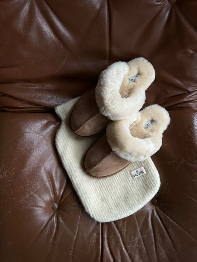 Wärmflasche mit Bezug aus Schurwolle liegt auf brauner Couch - Wollbebi